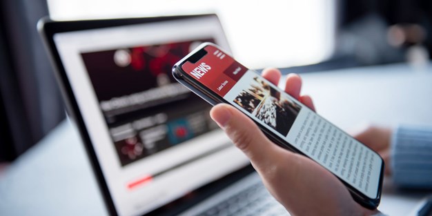A hand holding a smartphone and a laptop on a desk, photo.