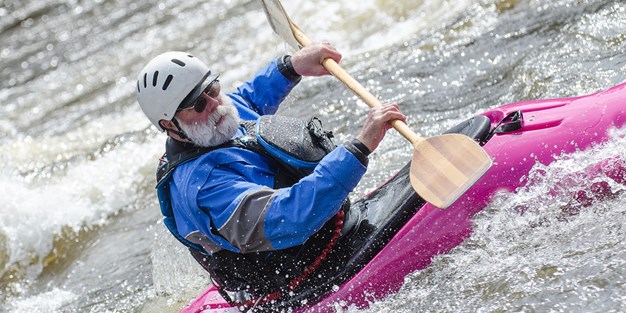 En äldre man som kör med sin kayak i en fors. Foto